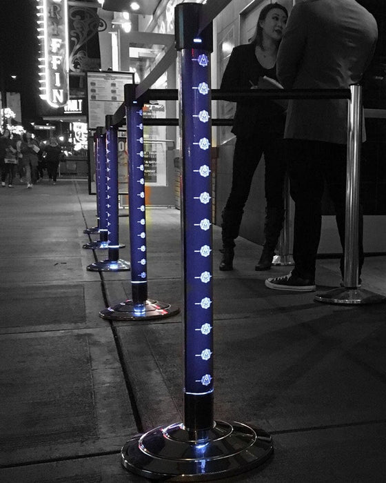 Queue management system with blue posts and black stands on a city street at night.